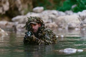 un' militare uomo o softair giocatore nel un' camuffare completo da uomo Sneaking il fiume e obiettivi a partire dal un' cecchino fucile per il lato o per obbiettivo. foto