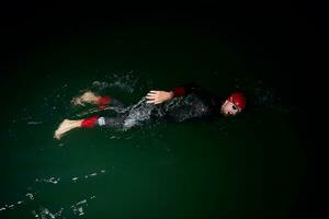 atleta di triathlon che nuota nella notte buia che indossa la muta foto