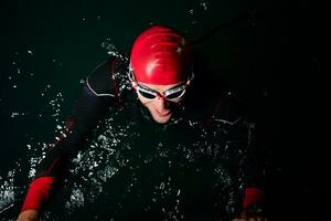 atleta di triathlon che nuota nella notte buia che indossa la muta foto