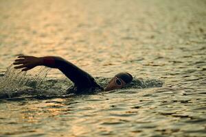 atleta di triathlon che nuota sul lago all'alba indossando la muta foto