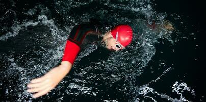 atleta di triathlon che nuota nella notte buia che indossa la muta foto