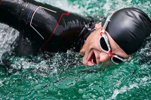 atleta di triathlon che nuota sul lago indossando la muta foto