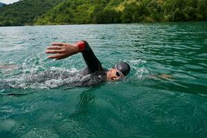 atleta di triathlon che nuota sul lago indossando la muta foto