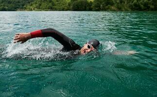 atleta di triathlon che nuota sul lago indossando la muta foto