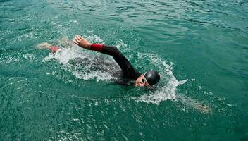 atleta di triathlon che nuota sul lago indossando la muta foto