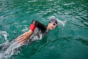 atleta di triathlon che nuota sul lago indossando la muta foto