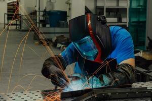 saldatore professionista dell'industria pesante che lavora all'interno della fabbrica, indossa il casco e inizia a saldare. messa a fuoco selettiva foto