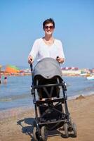 madre a piedi su spiaggia e spingere bambino carrozza foto