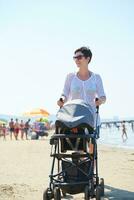 madre a piedi su spiaggia e spingere bambino carrozza foto