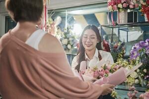 giovane asiatico femmina fioraio lavoratore nel grembiule consegna bellissimo fresco fiori mazzo per cliente chi acquistato ordine, contento venditore chi lavori nel colorato fiore negozio, e piccolo attività commerciale imprenditore. foto