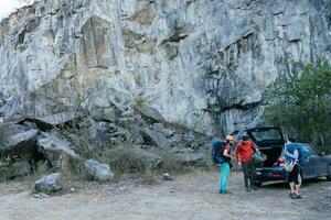 gruppo di giovane persone a il piede di il montagna scarico Ingranaggio a partire dal il auto per pratica roccia arrampicata. foto