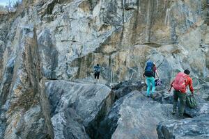 scalatori preparazione per salita. tre maschio femmina persone a piedi su il rocce. foto