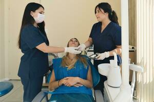 femmina dentista con un' Aiuto di sua assistente fissaggio denti di un' donna paziente nel il dentisti sedia. foto