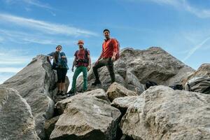 un' gruppo di arrampicata gli amici, sorridente e guardare a il telecamera a il superiore di il roccia. foto