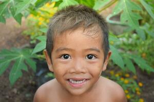 asiatico giovane ragazzo carino e affascinante guardare a il telecamera e sorridente felicemente su naturale sfondo avere impianti e fiori, bambini stile di vita, in alto vedere, chiudere alzato, sorridente con denti mostra, bambino. foto