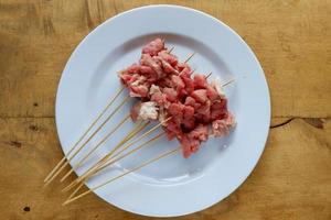 satay di capra cruda su piatto bianco con tavolo in legno foto