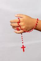 mano di un bambino con un rosario rosso foto
