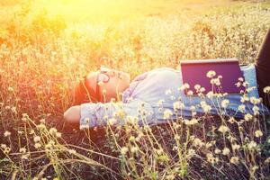 giovane donna hipster sdraiata in un campo di fiori dopo essersi stancata di leggere foto