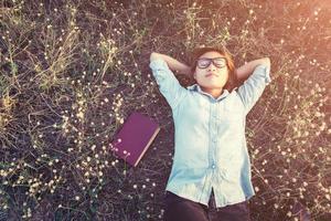 giovane donna hipster sdraiata in un campo di fiori dopo essersi stancata di leggere foto