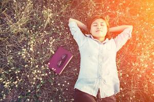 giovane donna hipster sdraiata in un campo di fiori dopo essersi stancata di leggere foto