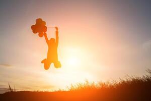silhouette di giovane donna che salta tenendo dei palloncini con il tramonto. foto