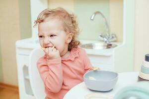 contento poco ragazza mangiare pasta nel scuola materna foto