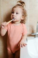 carino e divertente bambino ragazza spazzolatura sua denti nel il mattina nel il bagno foto