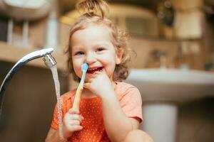 contento ridendo bambino ragazza spazzolatura sua denti nel il bagno foto