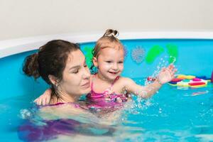 contento madre insegna sua poco figlia per nuotare nel il piscina foto