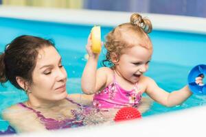 contento madre insegna sua poco figlia per nuotare nel il piscina foto