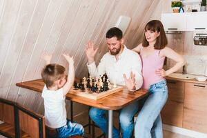 incinta mamma Guardando papà e figlio giocare scacchi a il tavolo foto