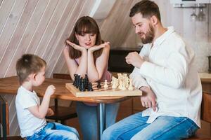 contento famiglia madre, papà e loro figlio giocando scacchi nel il camera foto