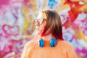 ritratto di un' giovane ridendo ragazza con bretelle ascoltando per musica nel cuffie nel il estate su il strada foto
