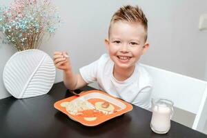 contento bambino mangiare delizioso pasta a il tavolo nel il cucina foto