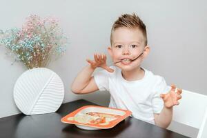 contento bambino mangiare delizioso pasta a il tavolo nel il cucina foto