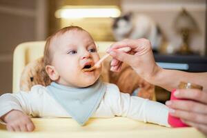 mamma feed un' contento bambino frutta puré a partire dal un' cucchiaio. primo cibo foto