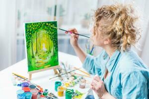 donna seduta nel davanti di un' pittura e pittura con spazzole su tela a casa foto