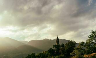 antico campana Torre nel un' medievale villaggio circondato di colline a tramonto foto