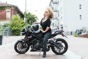 maturo motociclista donna lanci sua biondo capelli indietro equitazione il motociclo foto