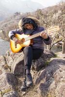 bellissimo maturo donna giocando un' chitarra seduta su un' roccia foto