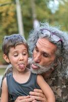 ritratto di padre con lungo grigio capelli e figlio siamo mostrando il lingua foto