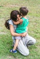 madre e figlio abbracciare amorevolmente su loro ginocchia nel un' verde parco foto