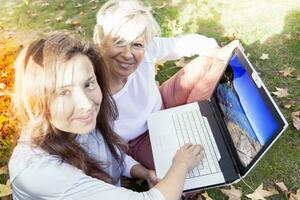 bella mamma e figlia consultare il il computer portatile sotto un' albero nel autunno foto