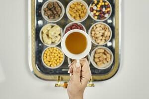 donna mani Tenere un' tazza di tè al di sopra di tradizionale Arabo iftar dolci e spuntini foto