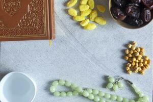 santo corano, rosario, iftar dolci e secco frutta con un' tazza di acqua. Visualizza a partire dal sopra. piatto posare foto
