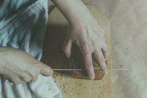casalinga taglio un' pane. femmina tagliare pane su taglio tavola. Visualizza a partire dal sopra. superiore Visualizza di pane foto