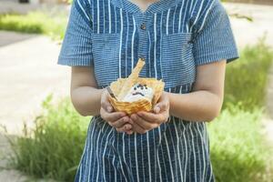 giovane donna Tenere delizioso ghiaccio crema con cialda durante un' picnic a natura. estate cibo concetto. giovane adulto mangiare delizioso ghiaccio crema con un' bastone su un' luminosa estate giorno. foto