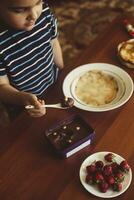 un' poco ragazzo con il suo madre preparazione insieme un' prima colazione. madre e figlio imbrattando cioccolato crema per magro Pancakes. gratuito spazio foto