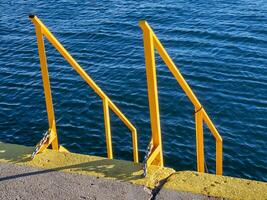 giallo le scale e corrimano su il banchine - in profondità blu mare nel il sfondo foto