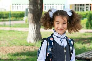 allegro divertente ragazza con un' sdentato Sorridi nel un' scuola uniforme con bianca fiocchi nel scuola cortile. indietro per scuola, settembre 1. contento allievo con un' zaino. primario formazione scolastica, elementare classe. foto